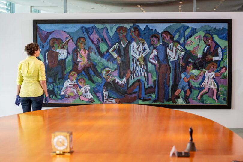 Foto: Eine Frau steht vor dem Gemälde „Sonntag der Bergbauern“ von Ernst Ludwig Kirchner im Kabinettssaal des Bundeskanzleramts.