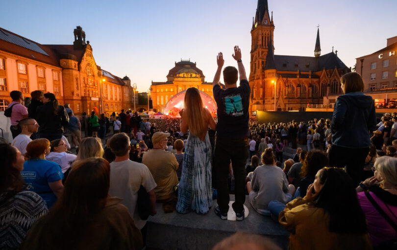 Zuschauer verfolgen des Auftritt der Rap-Rock-Band Kraftklub und der Robert-Schumann-Philharmonie zu Beginn des Kosmos-Festivals in Chemnitz. Das dreitägige Festival ist Teil des Programms von Chemnitz als Kulturhauptstadt Europas 2025. Es bietet rund 300 Programmpunkte.