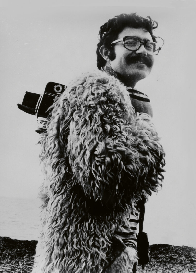Das Bild in schwarz weiß zeigt Toni Catany, der eine Kamera über der Schulter trägt.