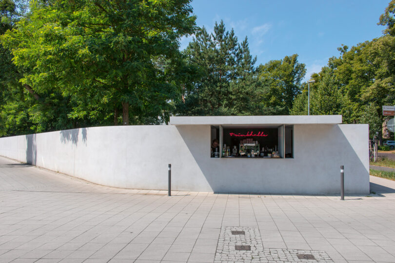 Die historische Trinkgalle befindet sich in einer weißen Mauer, dahinter sieht man grüne Bäume