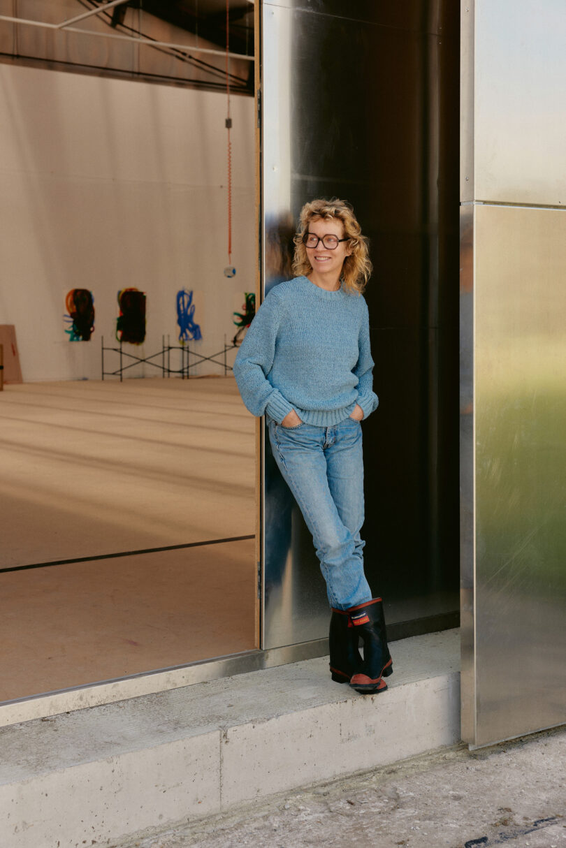 Katharina Grosse am Eingang zu ihrem Winteratelier in Jeans, Pullover und Gummistiefeln