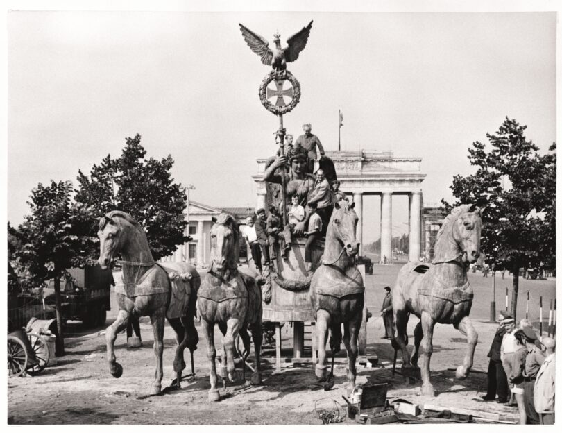 Personen sitzen auf der rekonstruierten Quadriga, die vor dem Brandenburger Tor steht.