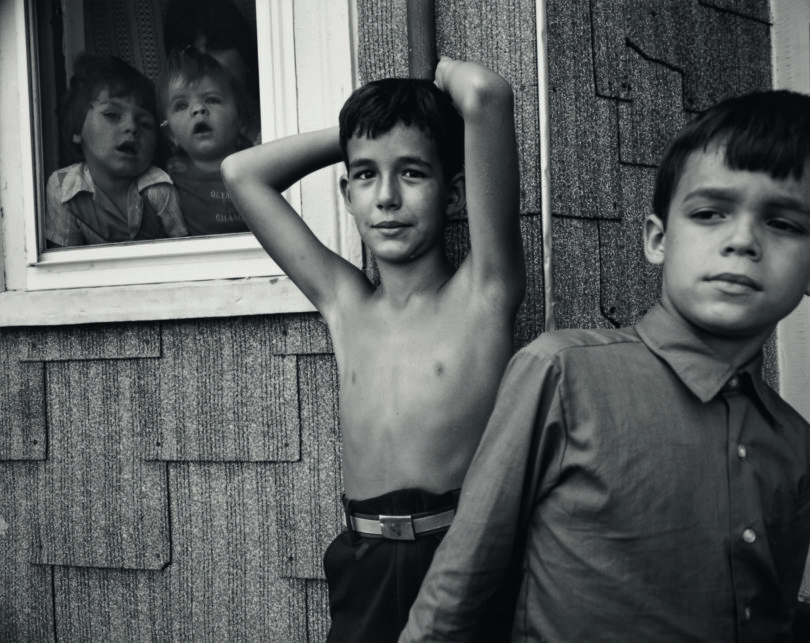 Vier Kinder werden in dieser schwarz-weiß Fotografie porträtiert, im Mittelpunkt eine Junge mit nacktem Oberkörper und sanftem Blick