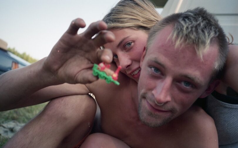 Intimes Portrait eines jungen Paares auf einem Festival, der Mann hält eine Miniatureisenbahn in die Kamera.